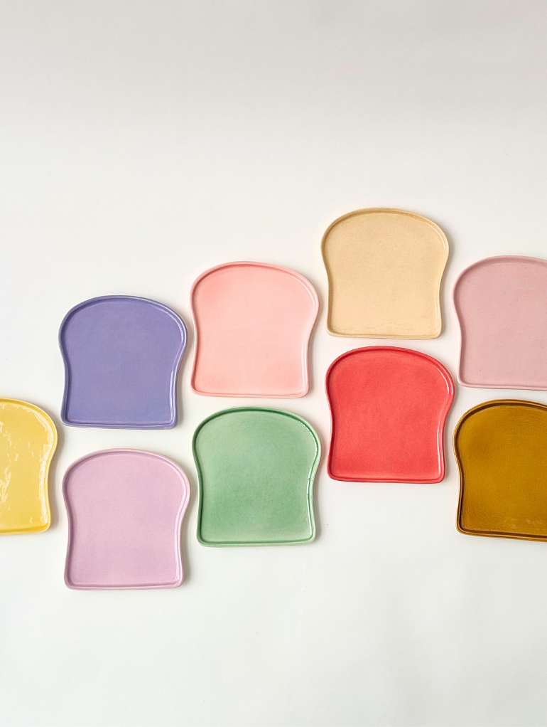 Useita värejä Munkaa Designin paahtoleivän muotoisesta Paahtis-leipälautasesta.